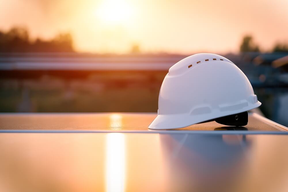 white worker helmet on a solar panel near a sunset