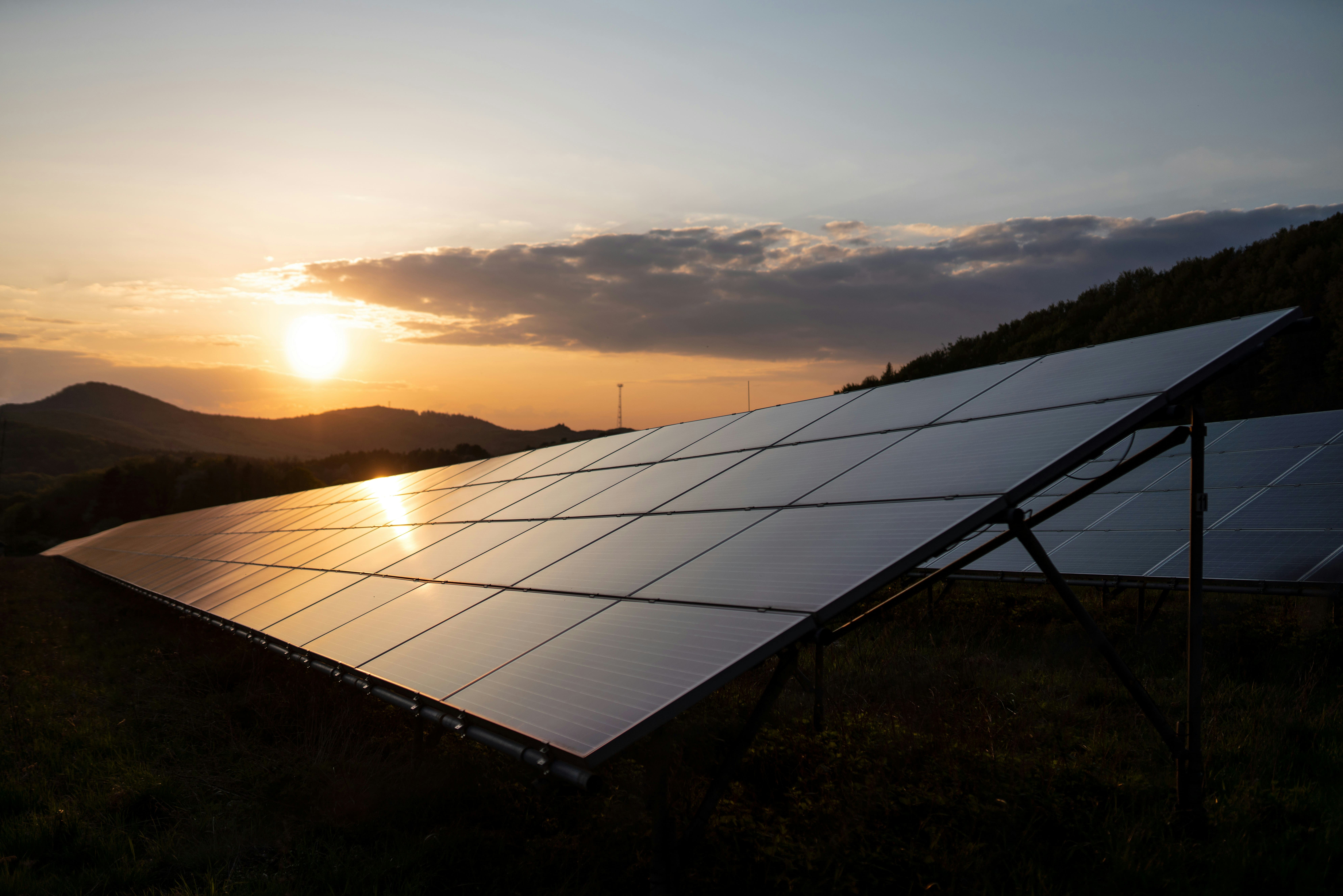 Solar panels in a rural setting with the sun setting behind hills, highlighting the potential for renewable energy systems supported by the REAP Grant.