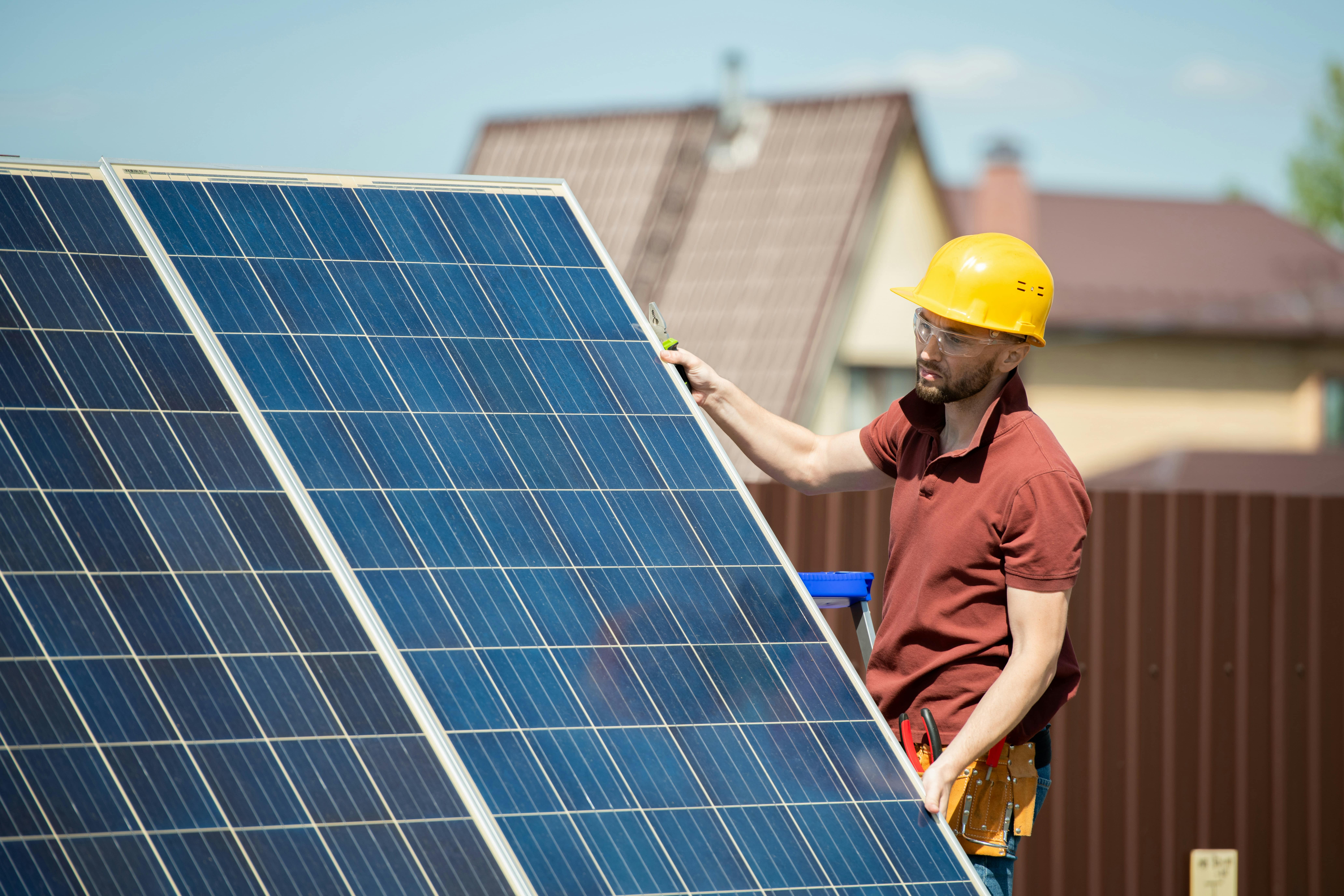 A technician in a hard hat performing maintenance on a solar panel, highlighting the importance of regular upkeep to manage depreciation and maintain efficiency.