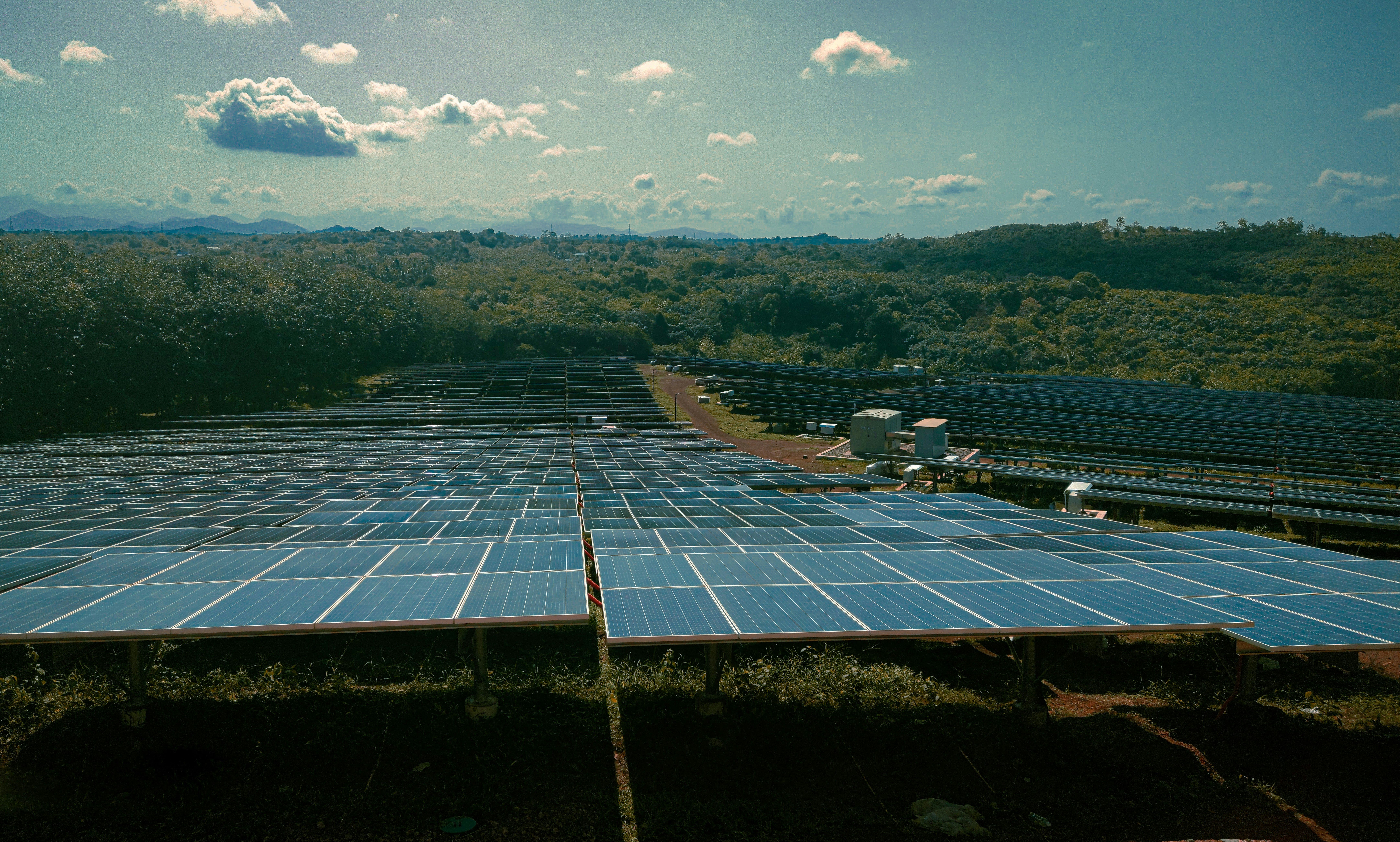 Expansive solar farm in a green, hilly area, illustrating the environmental benefits and large-scale implementation of commercial solar panels.