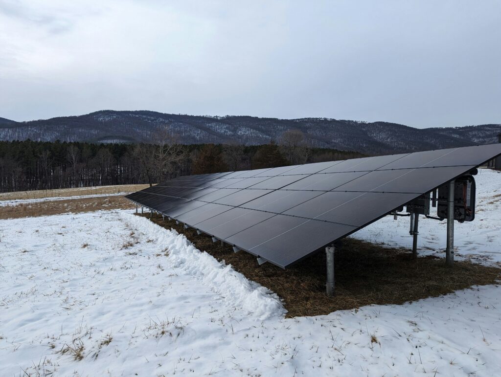 Solar panel array installed in a snowy field with mountains in the background, capturing the capability of solar power in midwest weather conditions.